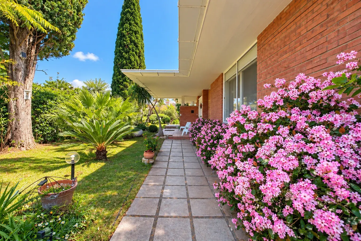 Path along the villa with a pink flowering hedge