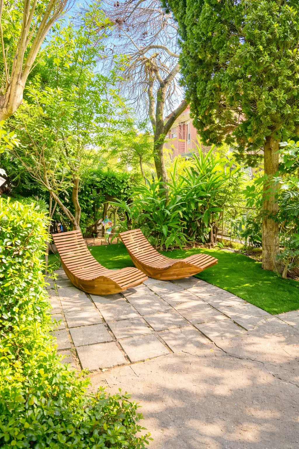 Two wooden rocking loungers among the greenery